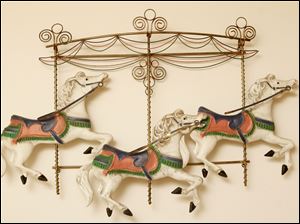 Collect-Call-Horses-Lynn-Burns-wall.jpg A metal sculpture of carousel horses dance on the wall.